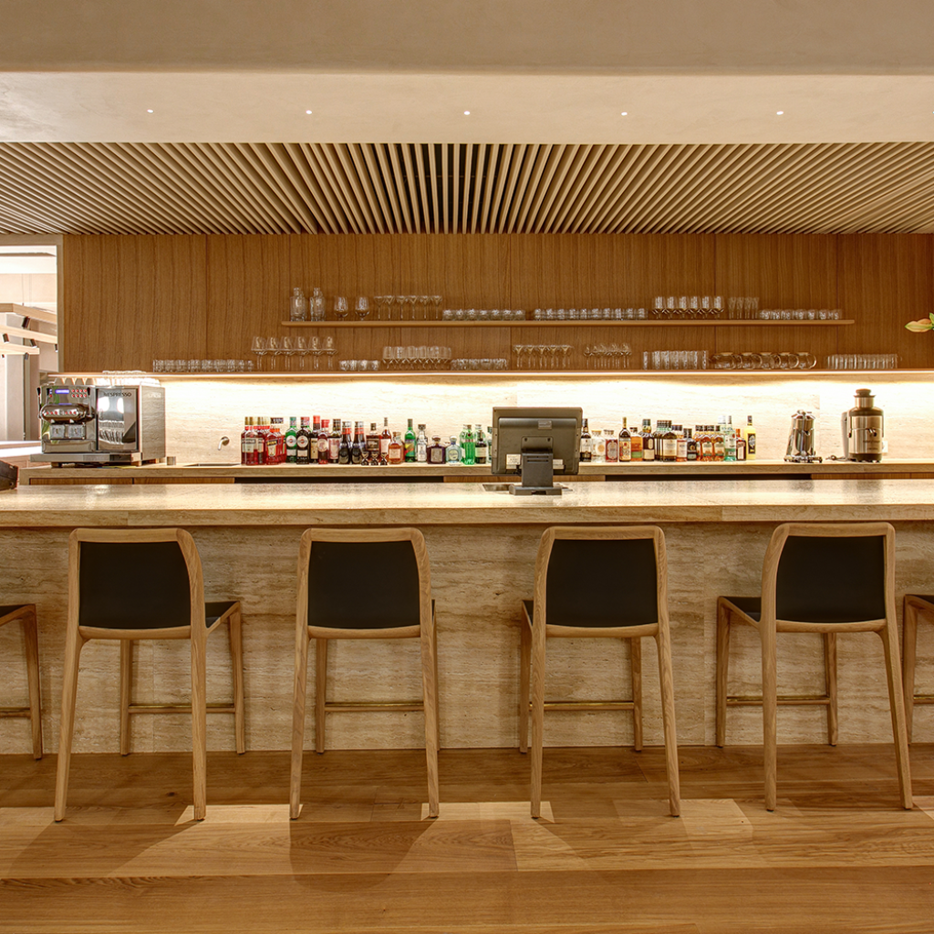 Tabourets de bar Invito Artisan en bois massif et cuir noir alignés devant un comptoir de bar