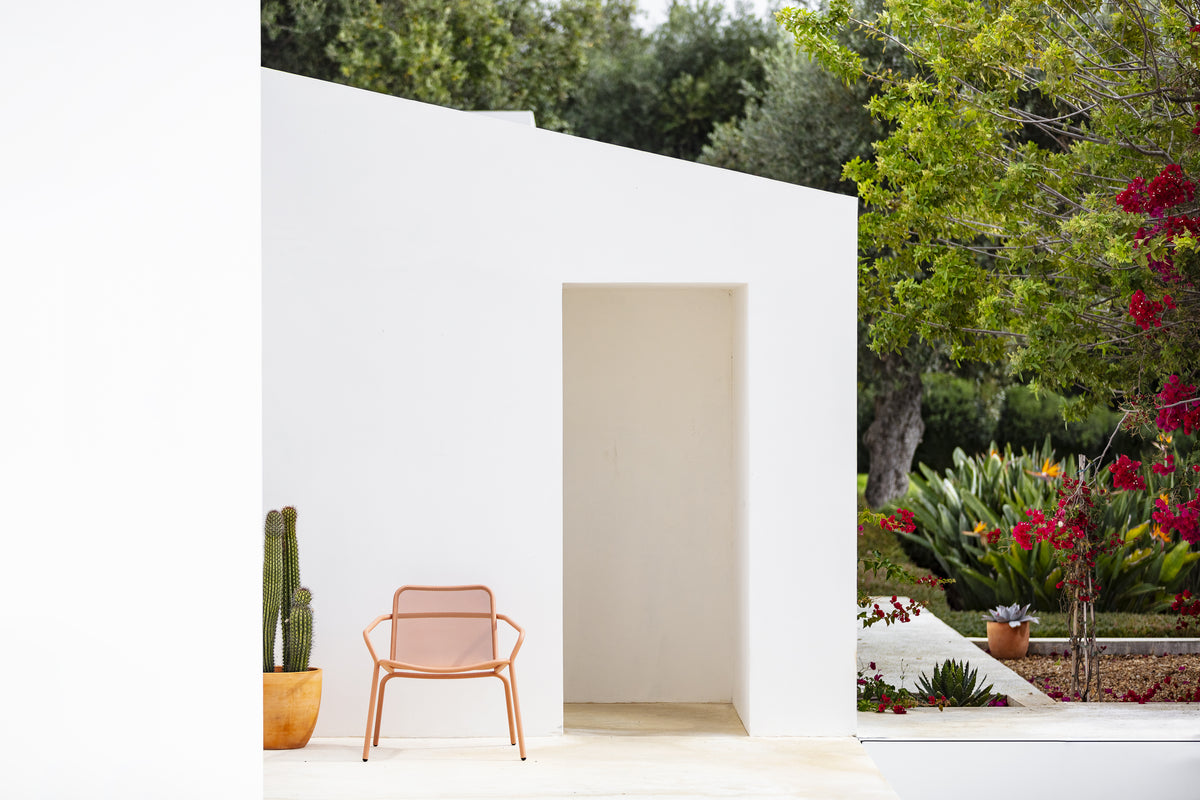 Fauteuil Starling Todus rose saumon devant un mur blanc dans un jardin